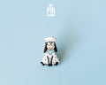 Hand-painted wooden sheep pin with a funny wide-eyed expression and a light blue bandana, finished with glossy resin