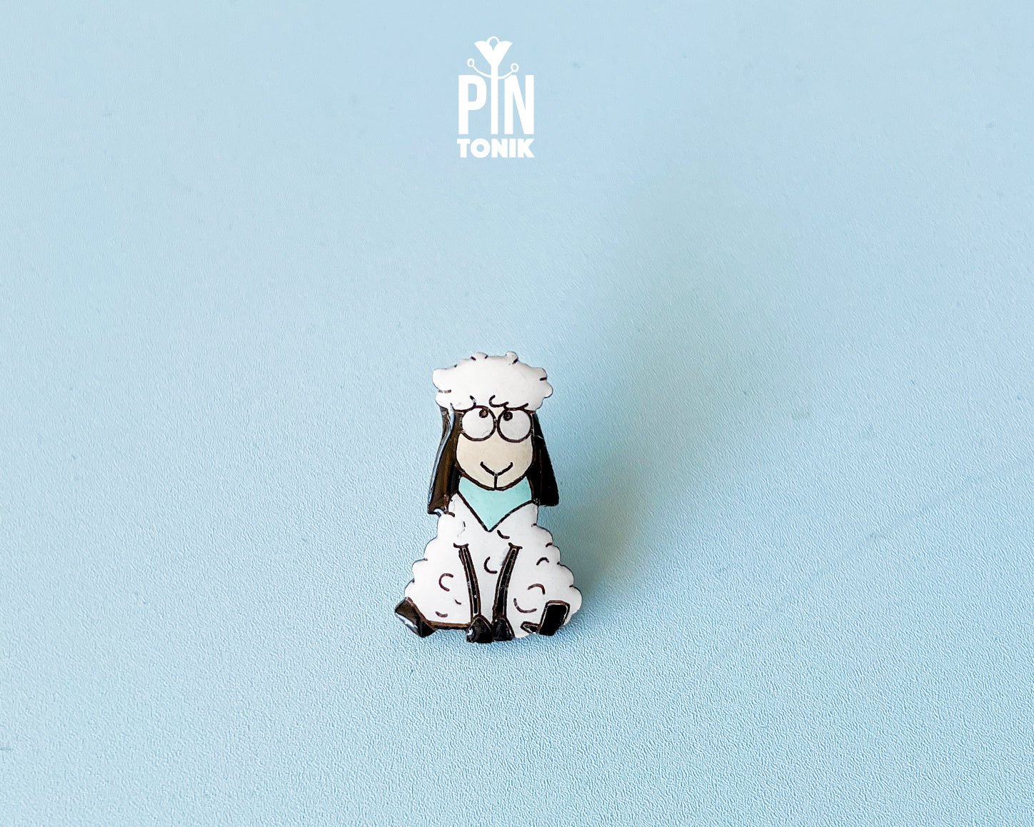 Hand-painted wooden sheep pin with a funny wide-eyed expression and a light blue bandana, finished with glossy resin