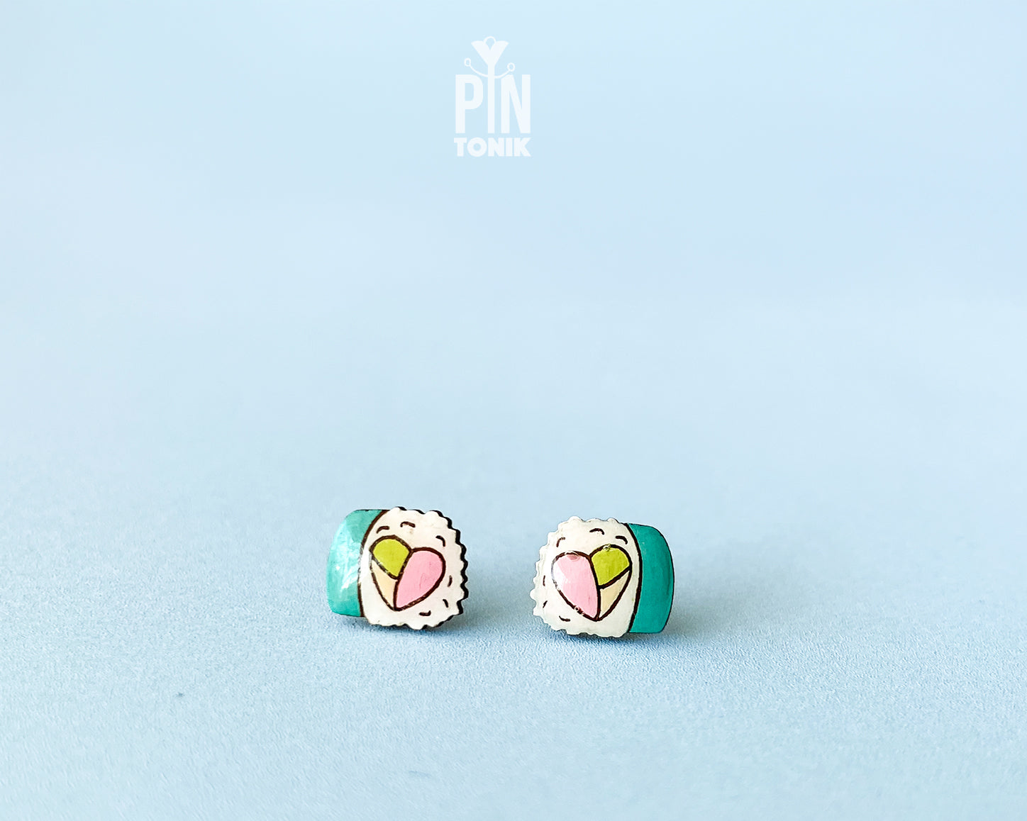 Handmade wooden sushi roll stud earrings showing a colorful pink and green filling wrapped in seaweed by PinTonik.