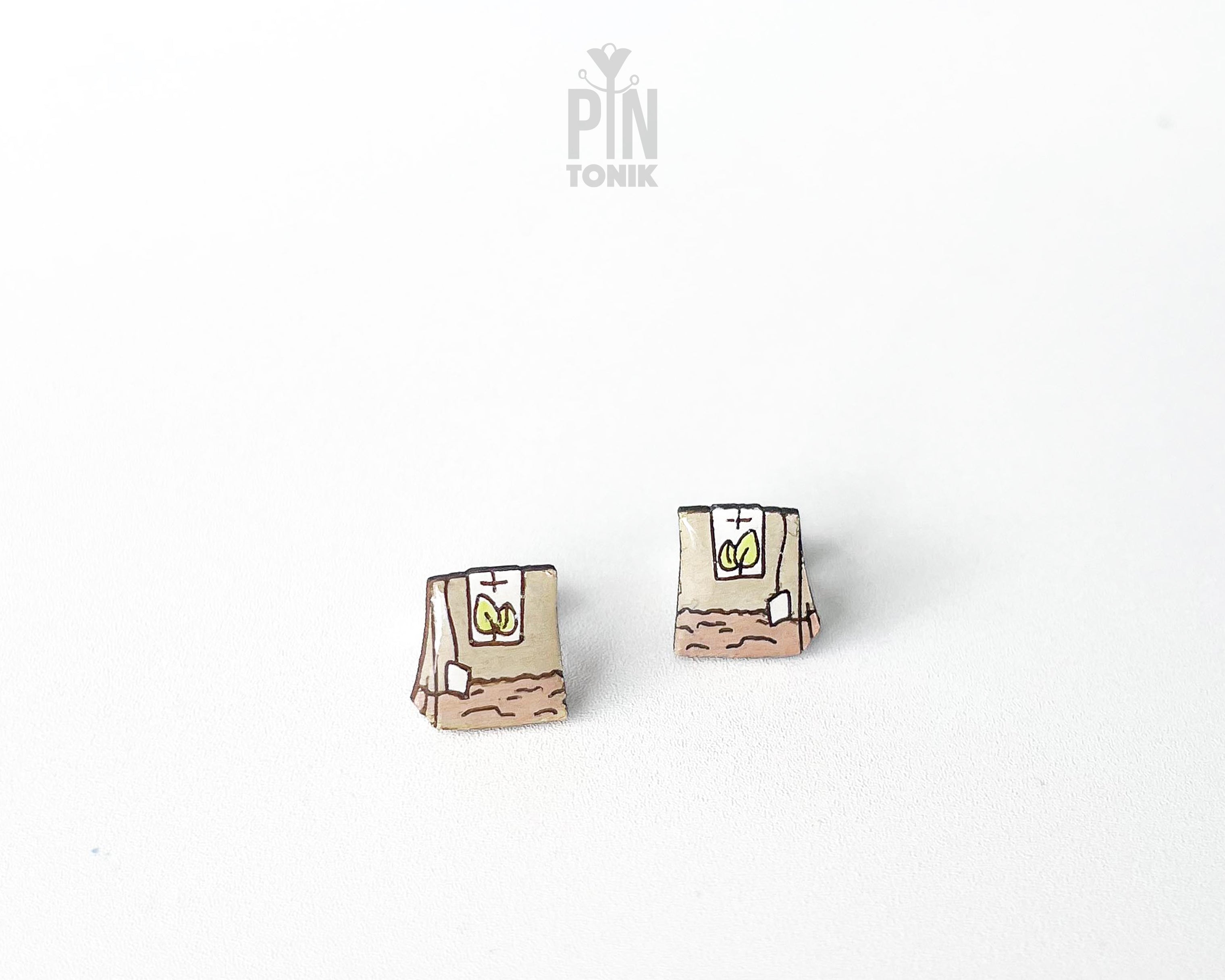 Handmade wooden tea bag stud earrings with a detailed paper bag texture, string, and tag illustration by PinTonik.