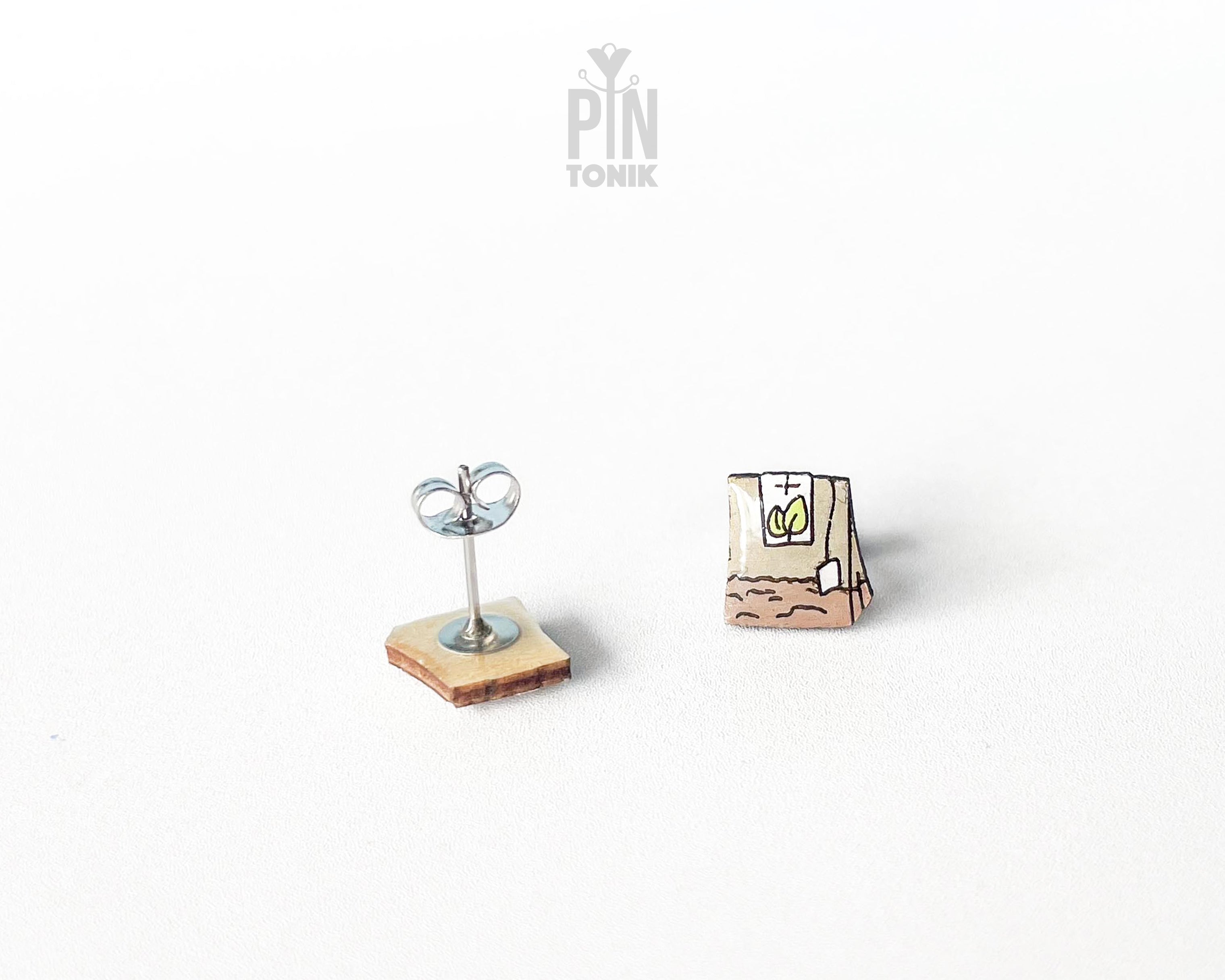 Handmade wooden tea bag stud earrings with a detailed paper bag texture, string, and tag illustration by PinTonik.