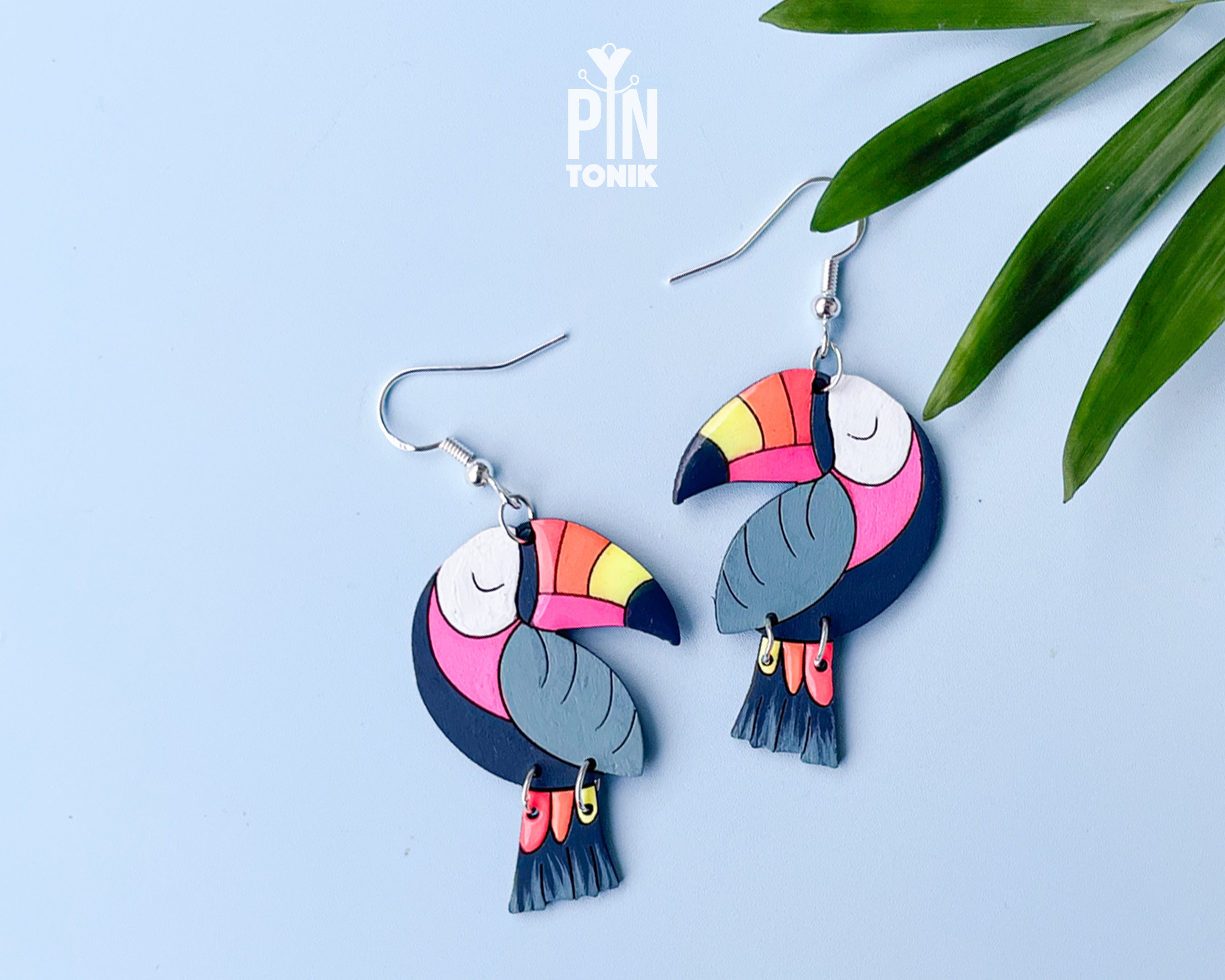 Large hand-painted wooden toucan dangle earrings with vibrant pink, yellow, and blue details on sterling silver hooks