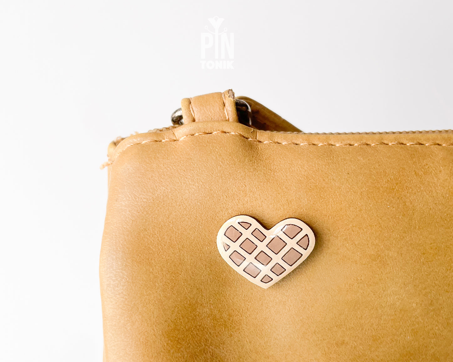Hand-painted wooden heart-shaped waffle pin with golden-brown detailing and a glossy resin finish, shown next to a gold-toned clutch back on a light blue background.