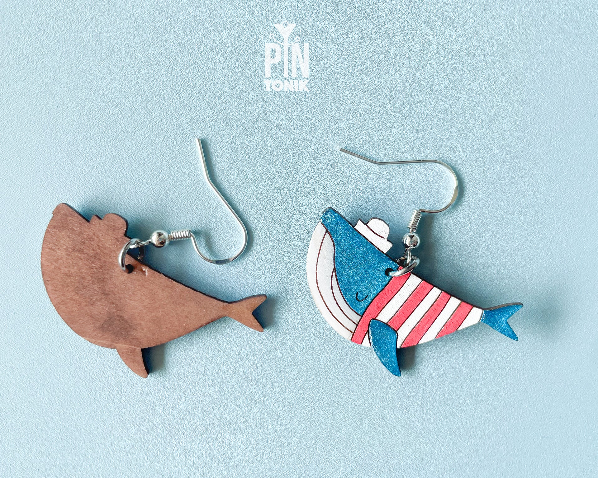 Hand-painted wooden blue whale dangle earrings wearing red and white striped sweaters and tiny sailor hats on sterling silver hooks