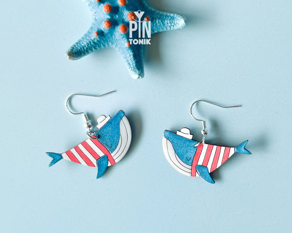 Hand-painted wooden blue whale dangle earrings wearing red and white striped sweaters and tiny sailor hats on sterling silver hooks