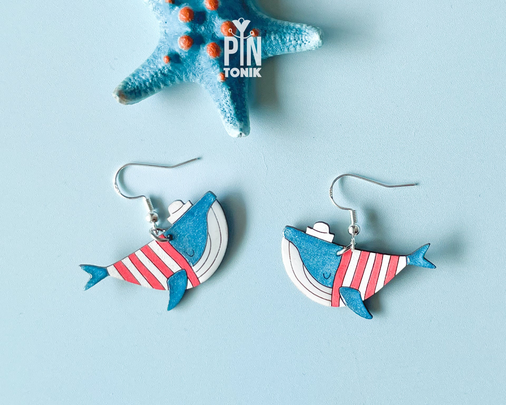 Hand-painted wooden blue whale dangle earrings wearing red and white striped sweaters and tiny sailor hats on sterling silver hooks