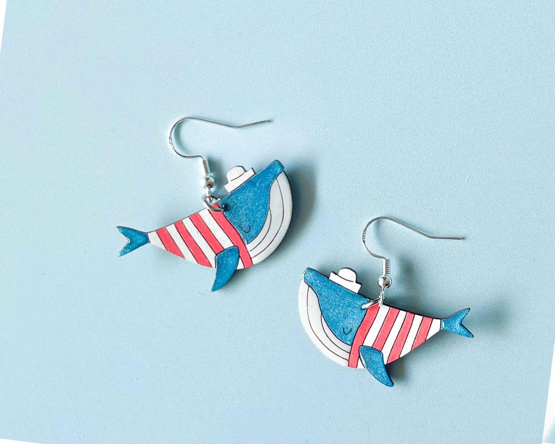 Hand-painted wooden blue whale dangle earrings wearing red and white striped sweaters and tiny sailor hats on sterling silver hooks