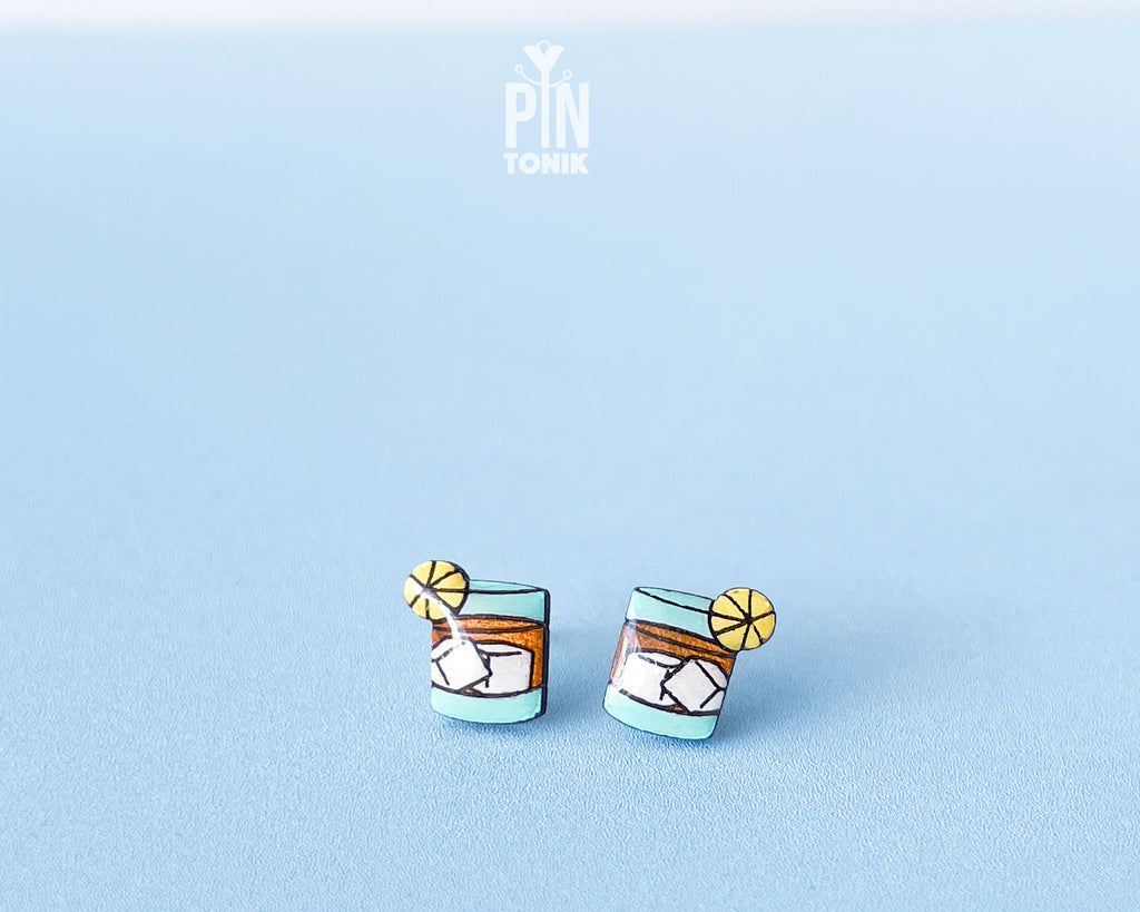 Handmade wooden cocktail tumbler stud earrings with a blue drink, ice cubes, and an orange wheel garnish by PinTonik.