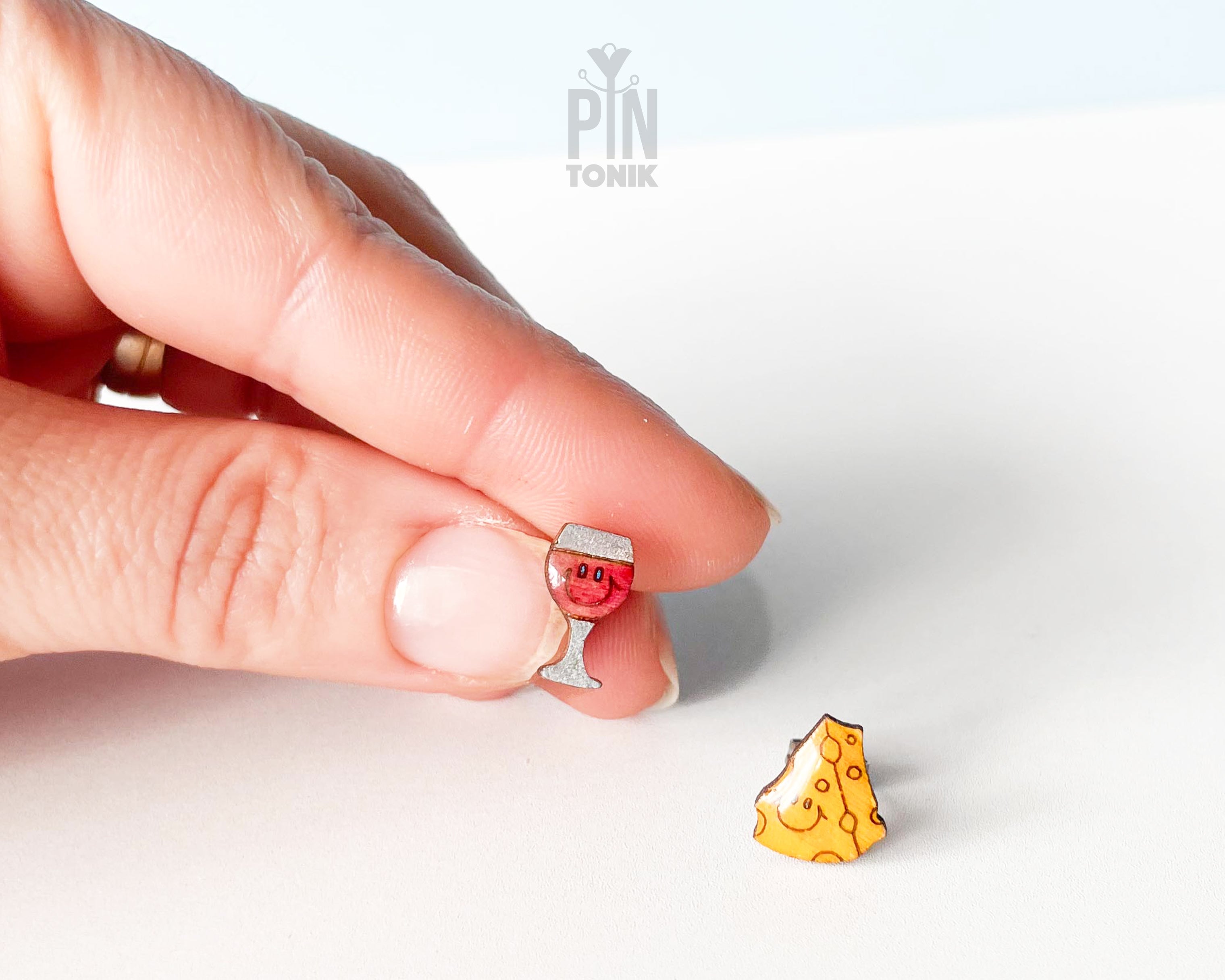 Handmade wooden mismatched stud earrings featuring a glass of red wine with a tiny smiley face and a happy, smiling yellow cheese slice by PinTonik.