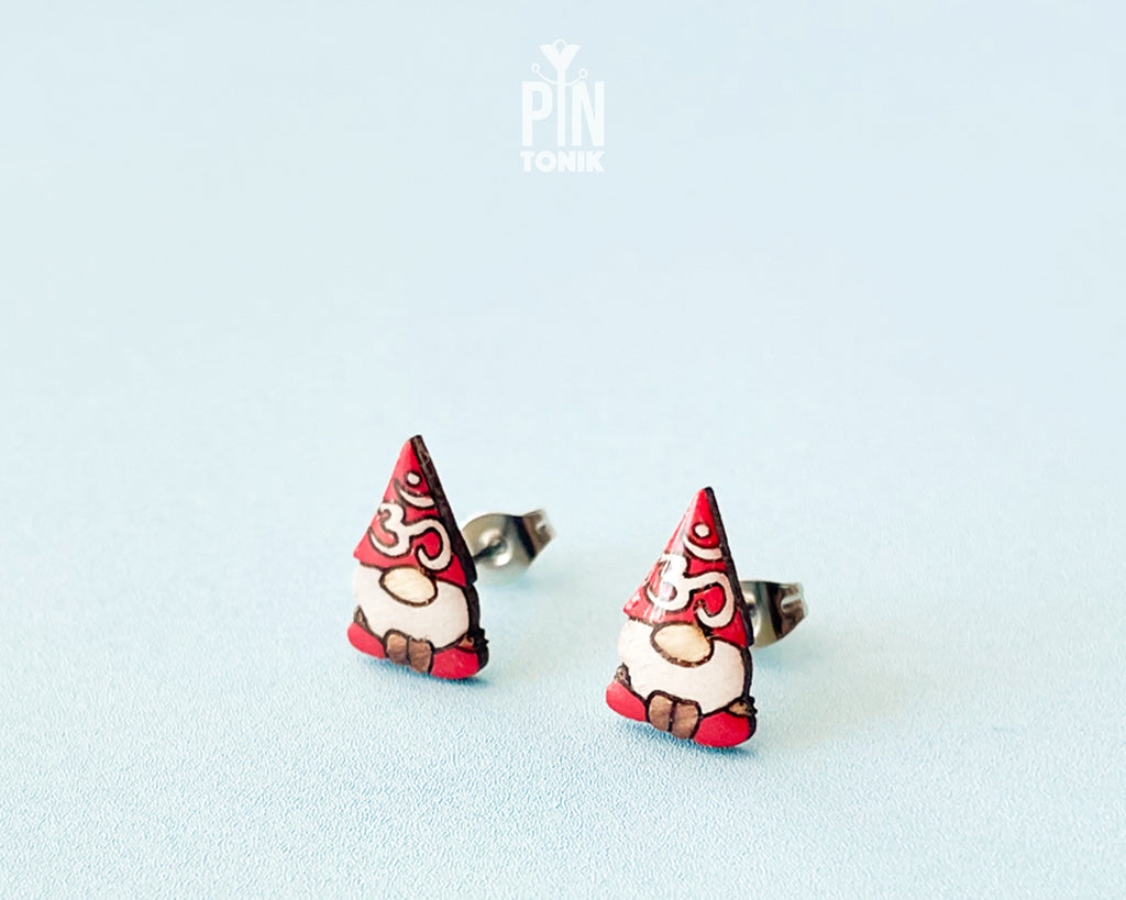 A pair of small gnome earrings. The earrings feature red hats with white Om symbol and brown shoes.