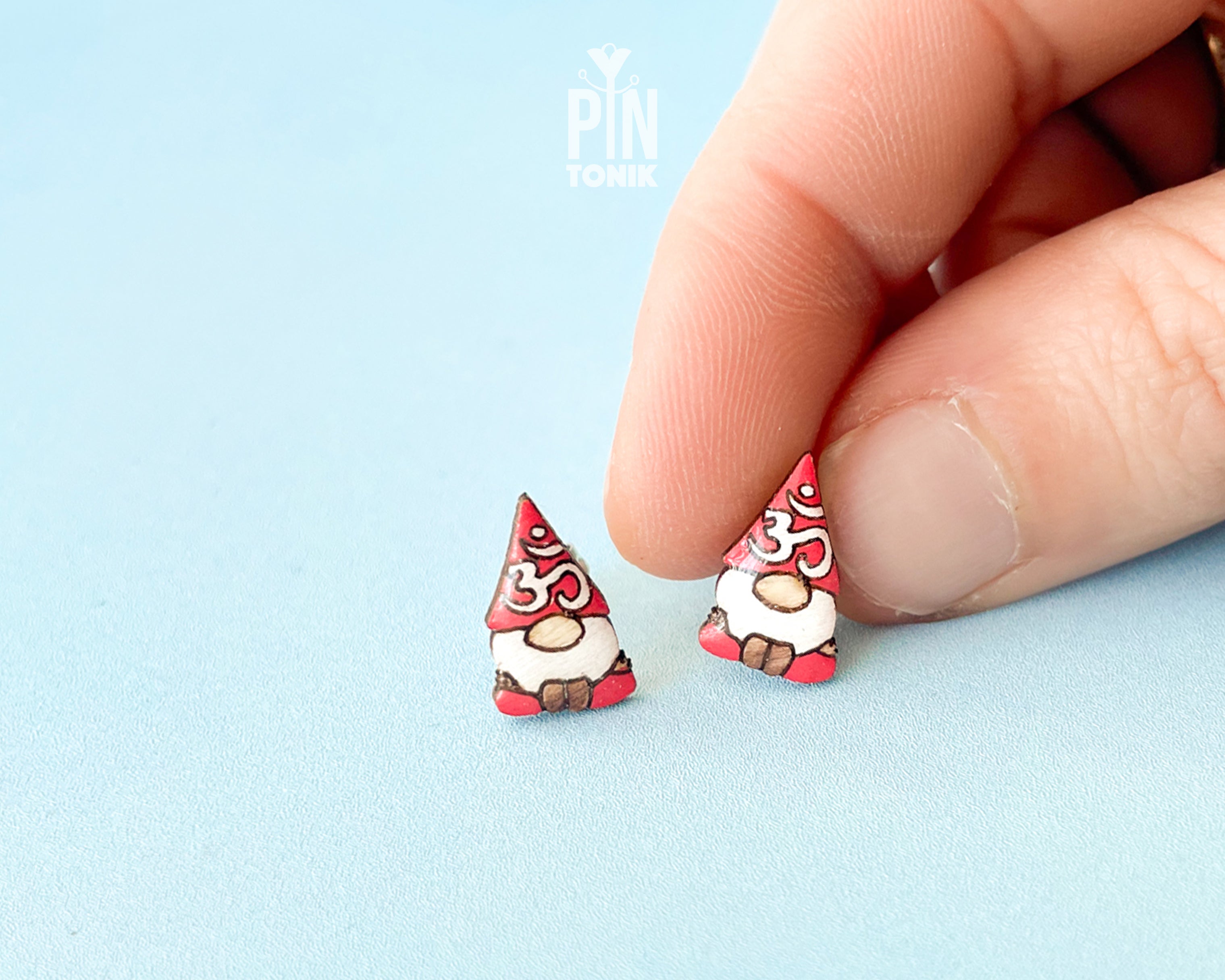A pair of small gnome earrings. The earrings feature red hats with white Om symbol and brown shoes.