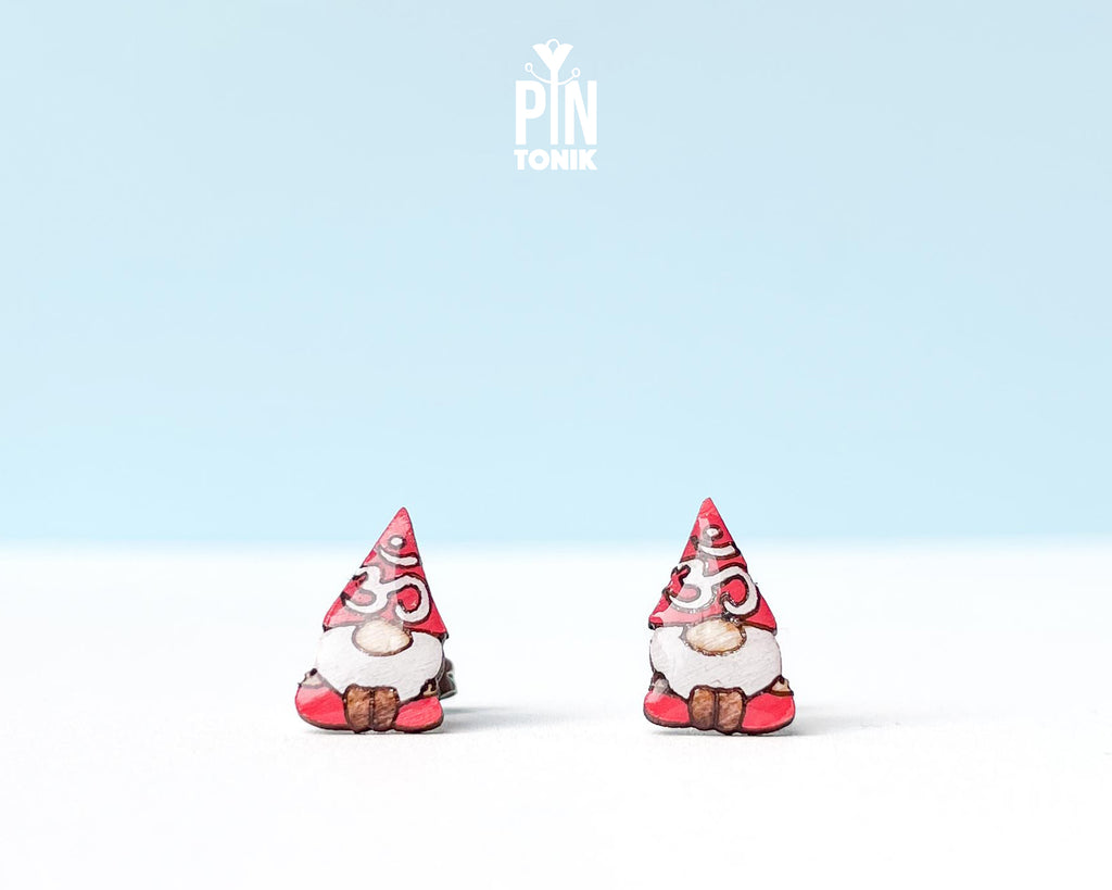 A pair of small gnome earrings. The earrings feature red hats with white Om symbol and brown shoes.