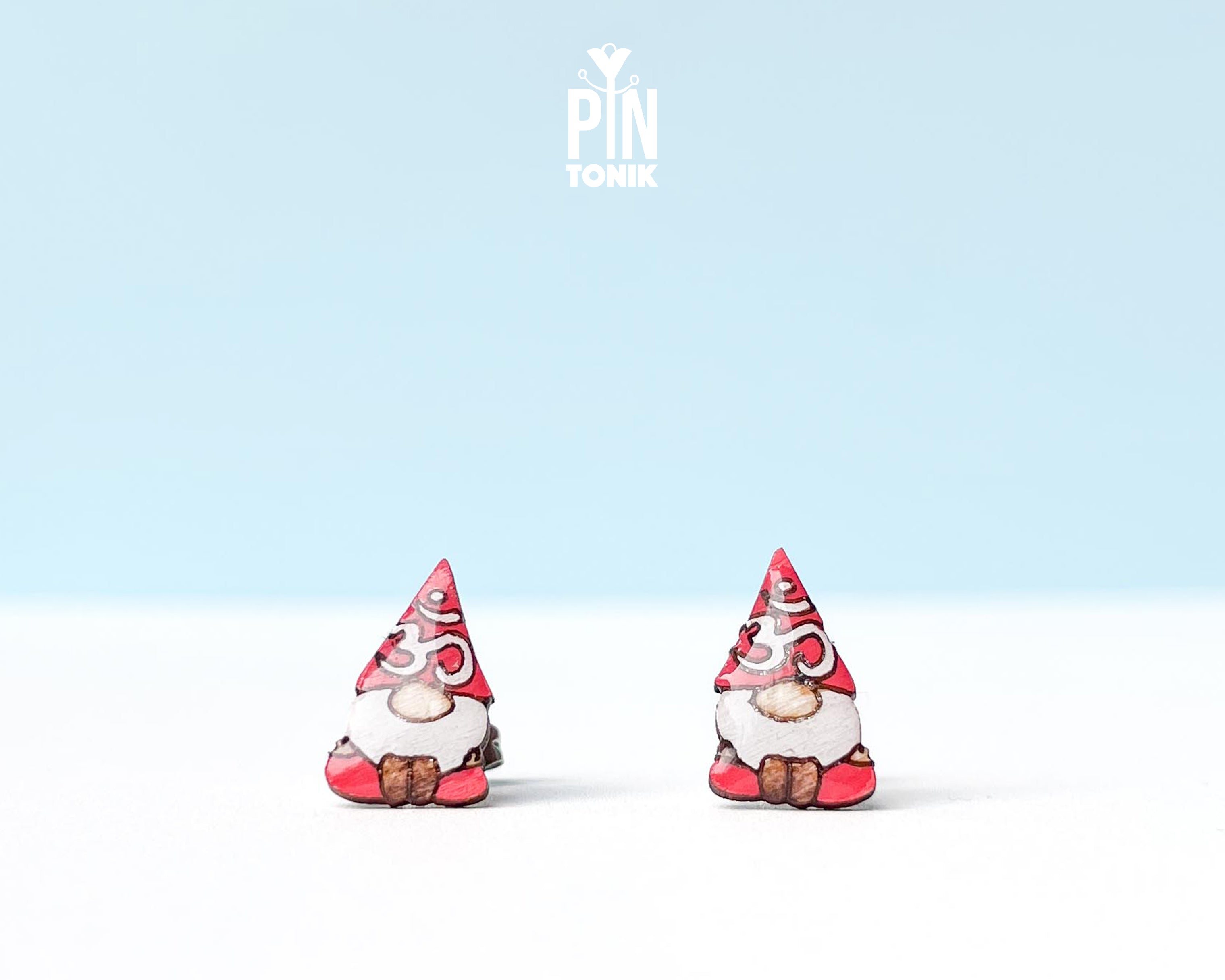 A pair of small gnome earrings. The earrings feature red hats with white Om symbol and brown shoes.
