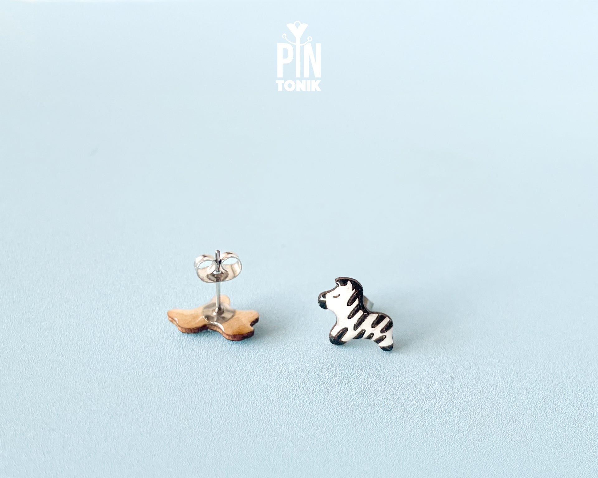 Pair of hand-painted wooden zebra stud earrings with black and white stripes and peaceful closed eyes