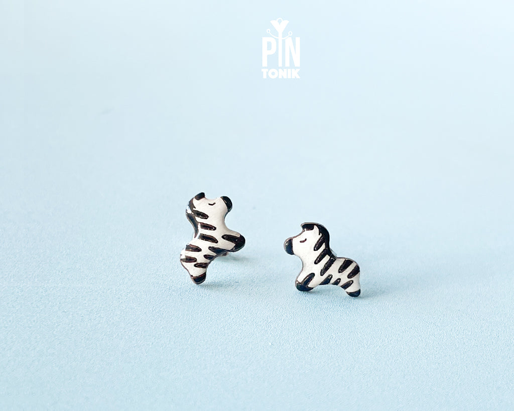 Pair of hand-painted wooden zebra stud earrings with black and white stripes and peaceful closed eyes