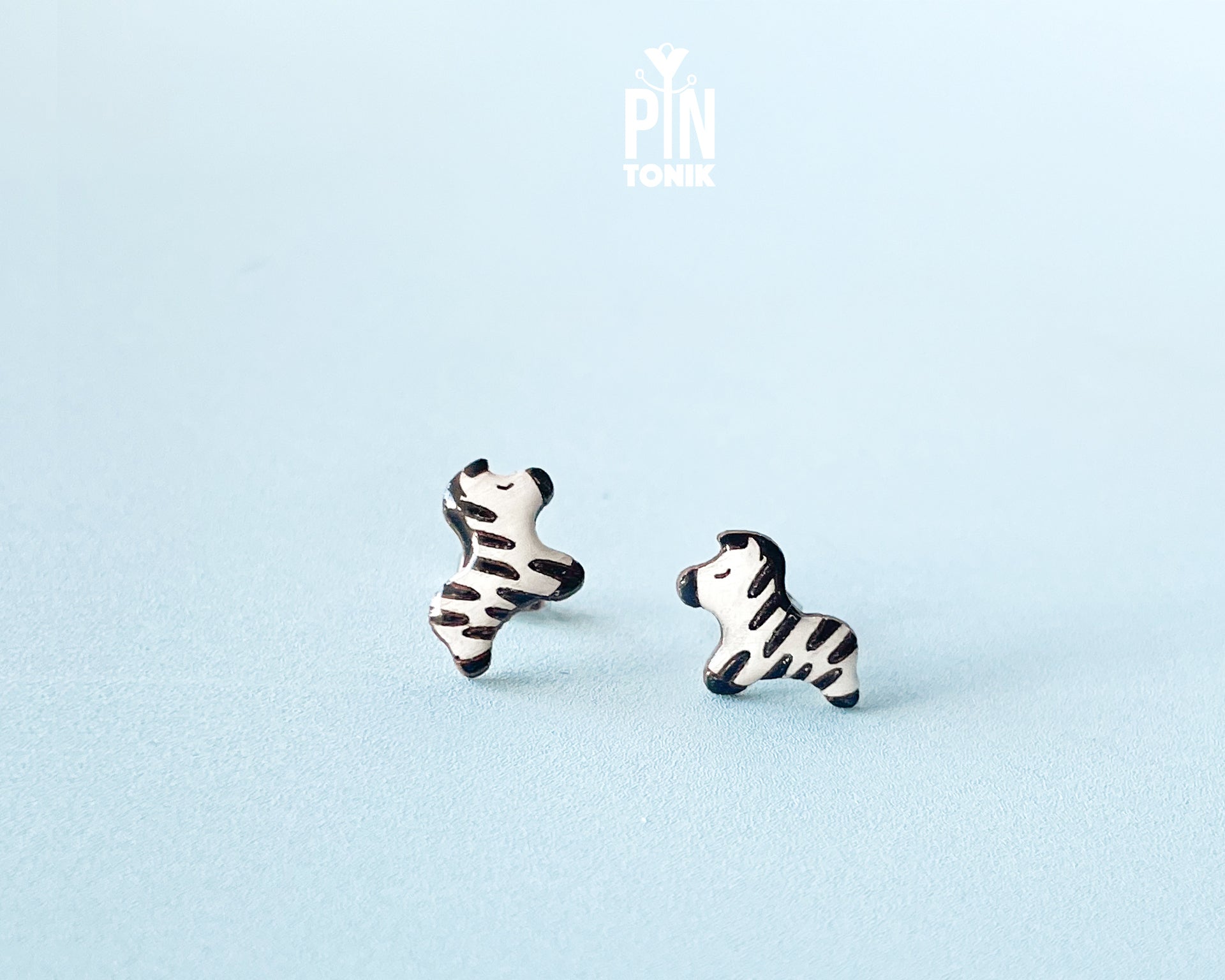Pair of hand-painted wooden zebra stud earrings with black and white stripes and peaceful closed eyes