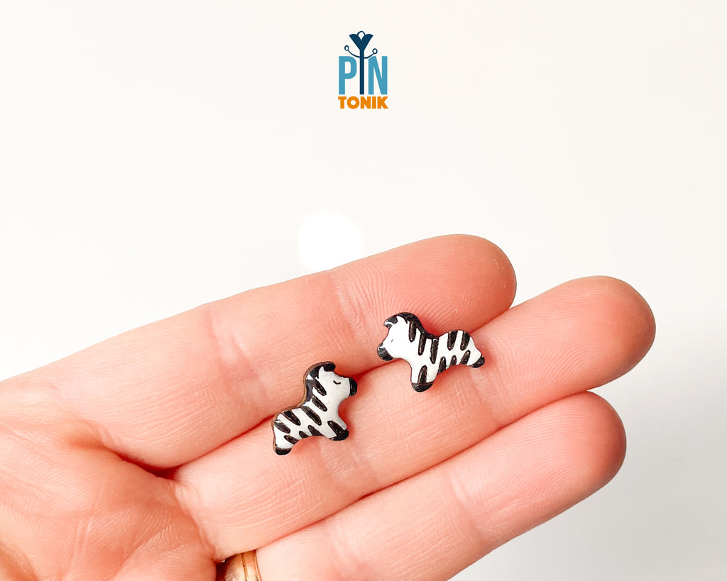 Pair of hand-painted wooden zebra stud earrings with black and white stripes and peaceful closed eyes