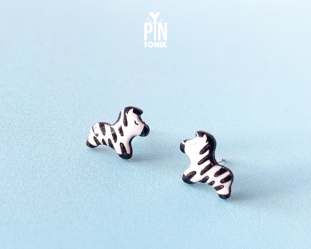 Pair of hand-painted wooden zebra stud earrings with black and white stripes and peaceful closed eyes
